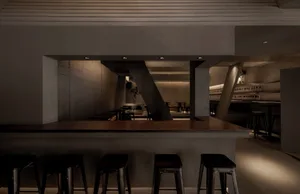 A minimalist industrial-style bar counter made of concrete, with stools in front of it and no customers.