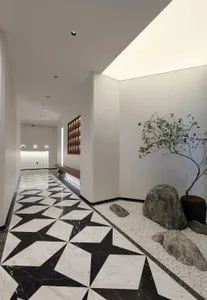 A modern entryway featuring black and white marble flooring, a small rock garden with a tree, and a long wooden bench against