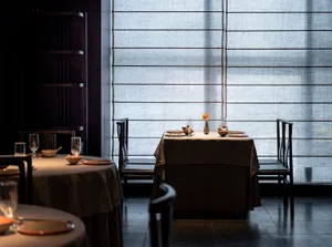 A minimalist restaurant interior featuring fabric curtains and wooden flooring.