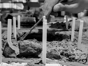 Hands using a tool to create a clay construction diorama with sticks and rocks.