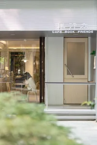A minimalist cafe interior featuring wood accents. There is a person sitting alone at a table. The shop is named Cafe Book Fr