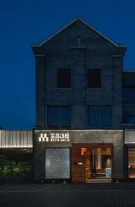 A modern restaurant with a brick exterior at dusk, featuring a lit sign and warm interior lights.