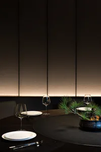 A modern black table setting with white plates, wine glasses, and a pine branch centerpiece.