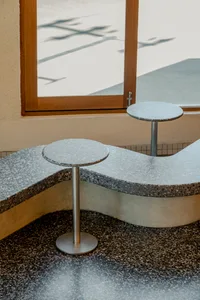 A modern coffee shop interior with a terrazzo countertop, featuring a unique curved seating design and metallic stools.