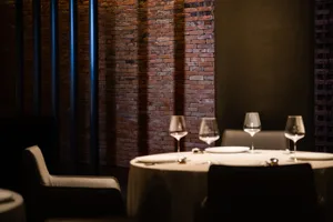 圓形餐桌擺設餐具與酒杯，背景為磚牆，搭配舒適的絨面座椅。