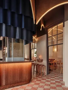 Interior of a modern restaurant with wooden bar counter, terrazzo flooring, and glass windows.
