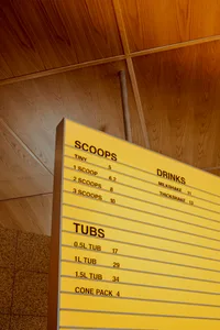 Yellow cardboard menu board with scoops and drinks prices.