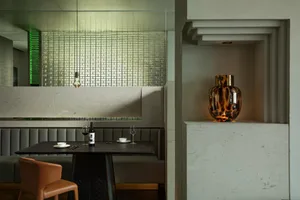A modern restaurant dining space featuring a sleek table setting with a bottle of wine on a black table, accompanied by a vas