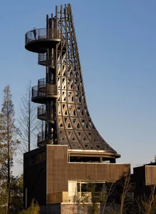A modern metal observation tower with a spiral staircase and a person standing at the top.