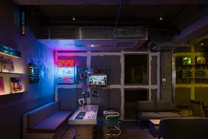 An industrial-themed bar area with metal furniture, concrete walls, and neon lighting.