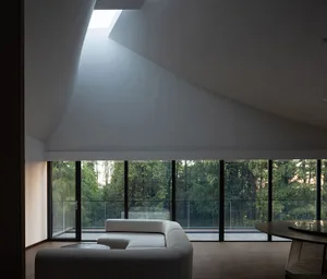 A modern living room featuring a concrete ceiling and floor, with large windows overlooking a forest.