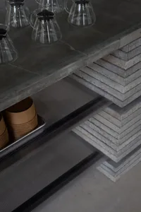Concrete kitchen counter and shelves with coffee pots and cups.