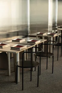 A sleek, modern restaurant interior featuring metal and black tables and chairs with red dishes.