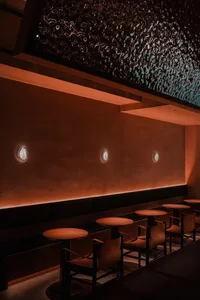 Modern restaurant interior with metal clad panel, orange chairs, and round tables.