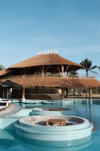 A poolside lounge area featuring a thatched-roof pavilion with wooden columns and seating.
