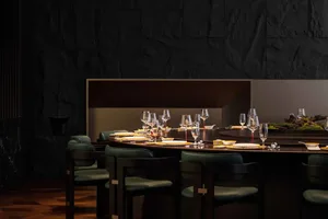 A modern restaurant interior featuring a circular dining table with black marble material and green chairs.
