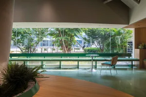 A modern cafe lobby featuring concrete walls and matte green seating against a large window with greenery outside.