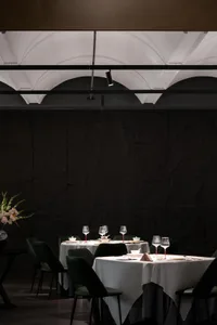 A restaurant interior with dark stone walls and white tablecloths on circular tables.