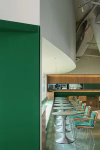 A modern restaurant interior with green chairs and tables and a wooden wall.