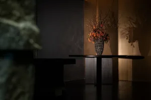 A modern interior showcases a metal table with a vase of orange flowers and twigs.
