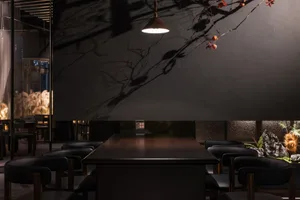 A modern restaurant interior with black walls, dark wood furniture, and a black stone counter, featuring a patterned glass pa