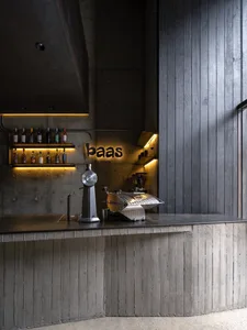 An industrial-style coffee shop bar featuring a concrete bar counter and illuminated shelves.