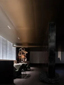 A minimalist restaurant interior with black, white, and metallic elements, featuring a modern hanging sculpture and a waterfa