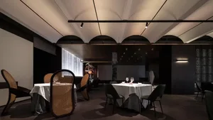 Modern restaurant interior with geometric arched ceilings, dark walls, and white tablecloths on tables.