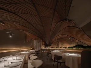 現代餐廳室內空間，木質天花板呈現波浪狀設計，餐桌採用昏暗燈光照明。