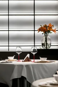 Modern restaurant table setting with white tablecloth, red-bottomed wine glasses, and orange lilies in a vase.