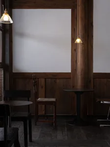 A cafe interior featuring wooden walls and tables, with pendant lights hanging above.