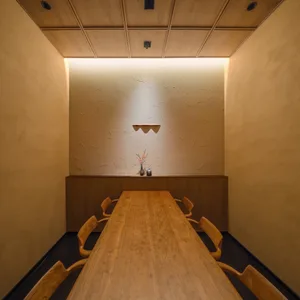 A minimalist restaurant interior featuring a long wooden table and chairs.