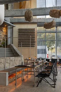 Industrial-style restaurant with minimalist design, concrete walls, and hanging plant baskets.