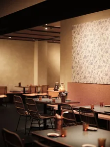 Interior view of a restaurant showcasing wooden tables, fabric chairs, and floral wallpaper.