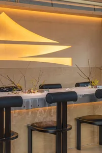 A sleek, minimalist restaurant interior featuring wooden fixtures and modern lighting.