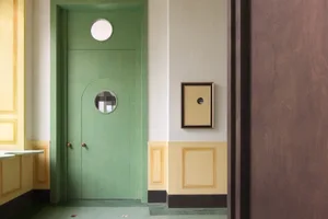 A minimalist interior design featuring a wall painted in soft green with a wooden frame and a small window.