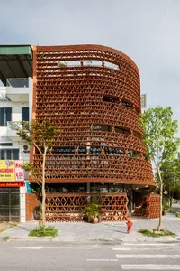 A modern building with a unique metal mesh facade and greenery on top.