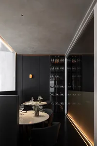 Modern dining room with black metallic wall featuring round tables and chairs, illuminated by subtle ambient lighting.