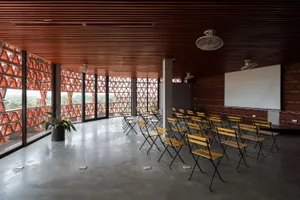 A modern industrial conference room with wooden chairs, metal tables, and concrete floor.