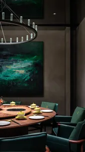 Modern restaurant interior featuring a round wooden dining table with green chairs and minimalist decor.