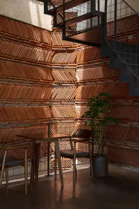 A cozy wooden coffee shop interior with a modern design, featuring a wooden table and chairs, a green plant, and a geometric 