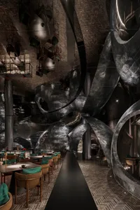 A modern, industrial restaurant interior with metallic and textured walls, featuring tables and chairs.