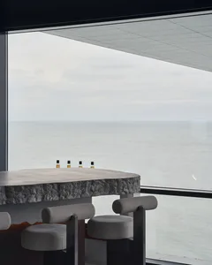 A minimalist bar area with concrete stools and glass elements, overlooking the ocean.