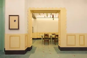 Interior of a cafeteria with yellow painted walls, wooden furniture, and green flooring.