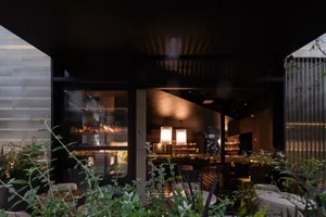Modern restaurant interior with concrete walls, glass windows, and a bar area.