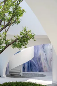 An outdoor modern architectural space featuring a white curved staircase and wall with a mix of blue and purple hues.