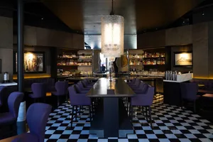 Interior of a modern bar featuring black marble countertops and a high ceiling with a large cylindrical light fixture.