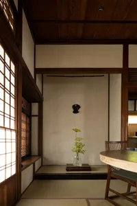 A modern living room interior with wooden walls and floor, featuring a vase with green flowers on a low table and a window wi