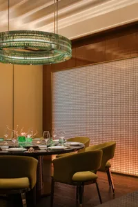 An industrial-style restaurant interior with black marble table, green glass chandelier, and green upholstered chairs.