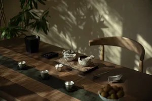 A wooden table with ceramic tea pots and cups, surrounded by greenery and natural light.